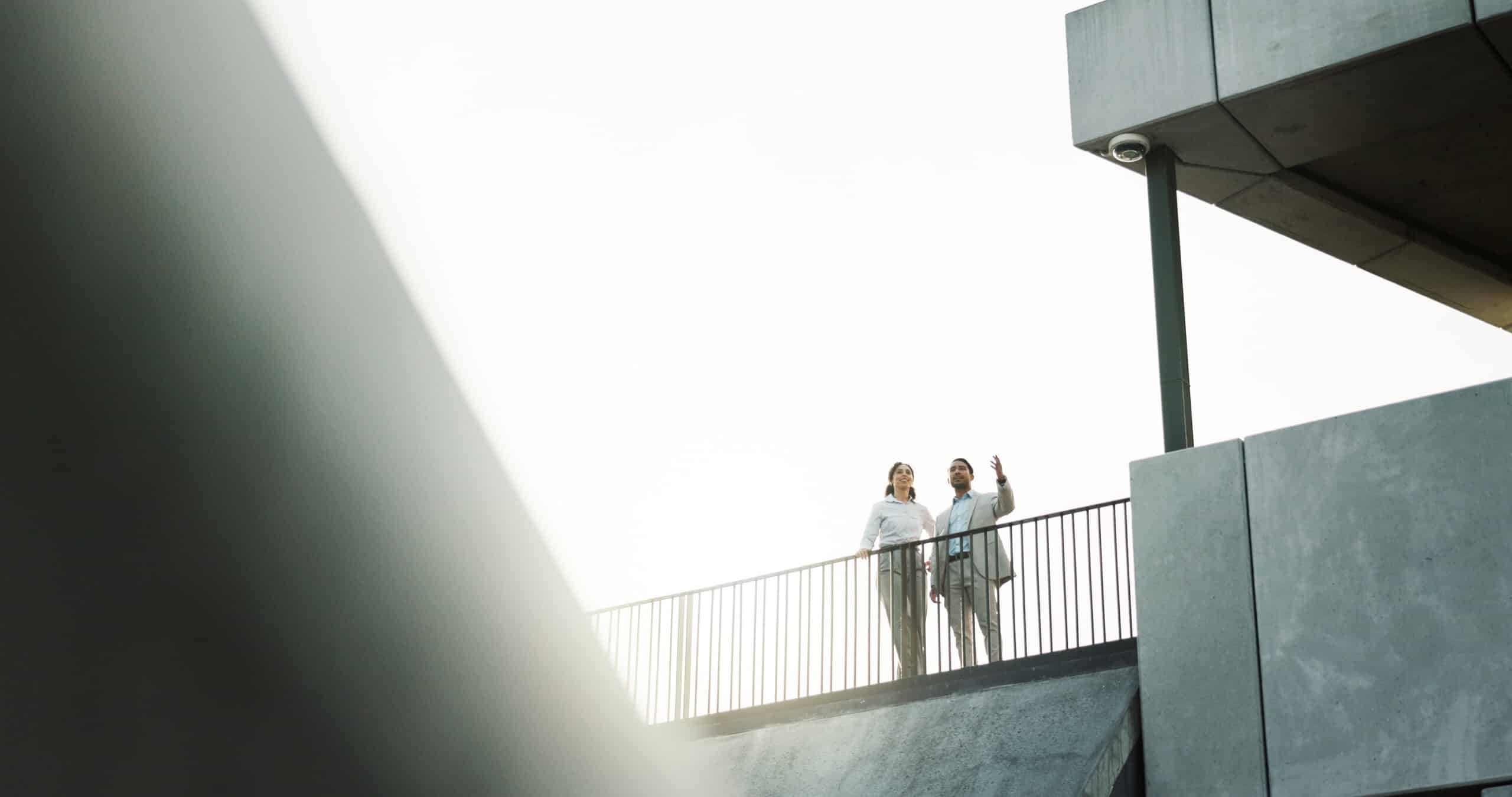 Immobilienbewertung: Objekt und Lage im Blick Zwei Personen im Businessoutfit stehen auf der Terrasse eines Gebäudes und betrachten die Umgebung