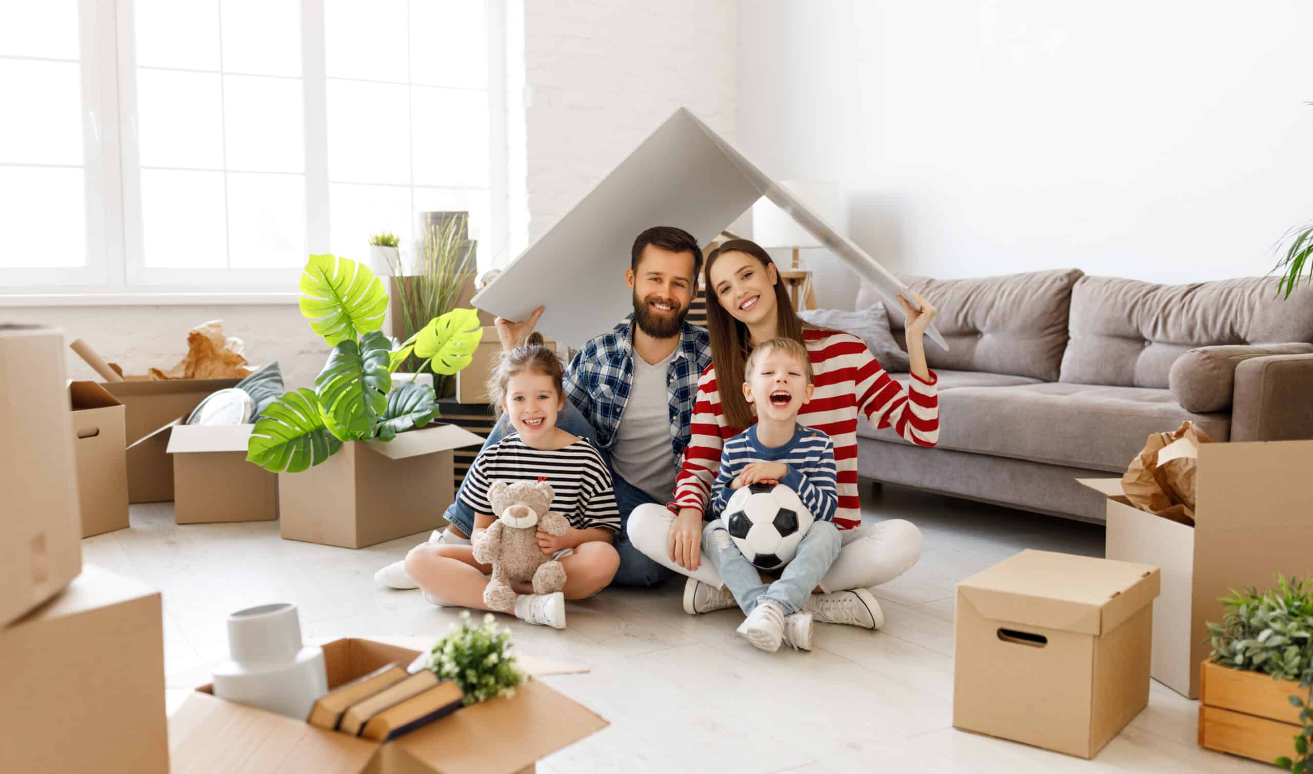 Familie im neuen Zuhause Familie mit zwei Kindern sitzt zwischen Umzugskartons im neuen Wohnzimmer.