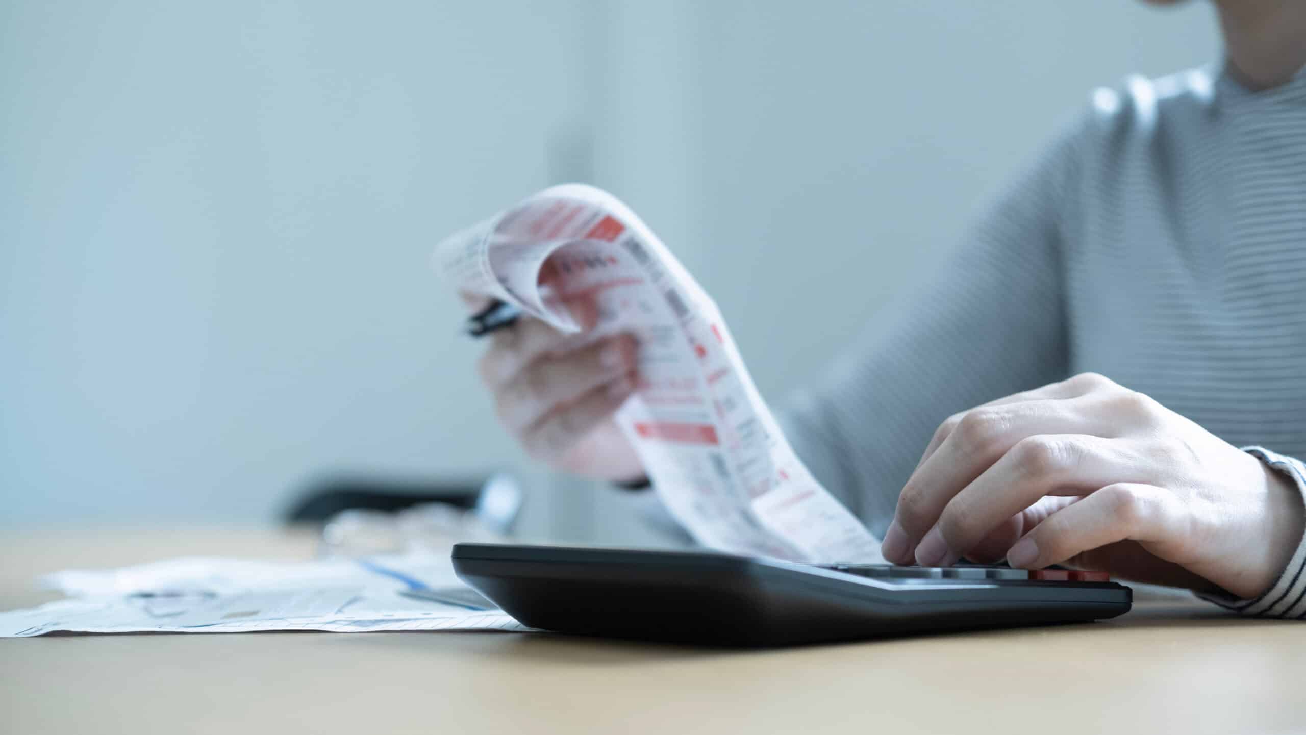 Forderungen prüfen und Haushaltsplan erstellen Person tippt auf einem Taschenrechner und prüft dabei eine lange Rechnung mit roten Mahnhinweisen