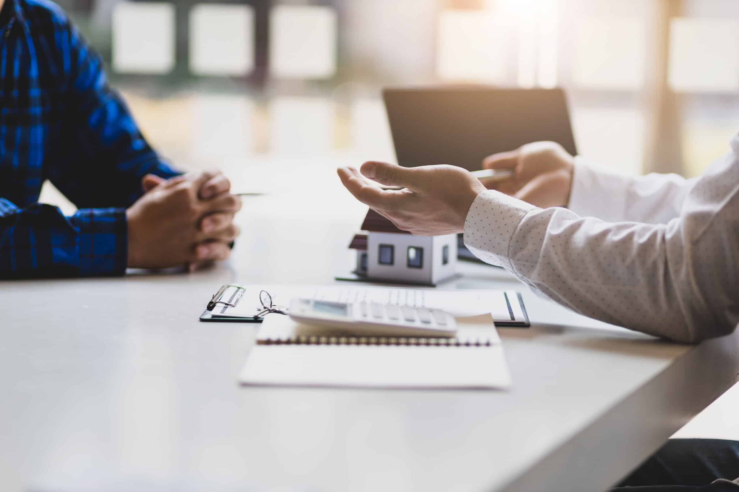 Ertragswert berechnen: Beratung zur Immobilienbewertung Beratungsgespräch am Tisch mit Hausmodell, Taschenrechner und Unterlagen zur Immobilienbewertung
