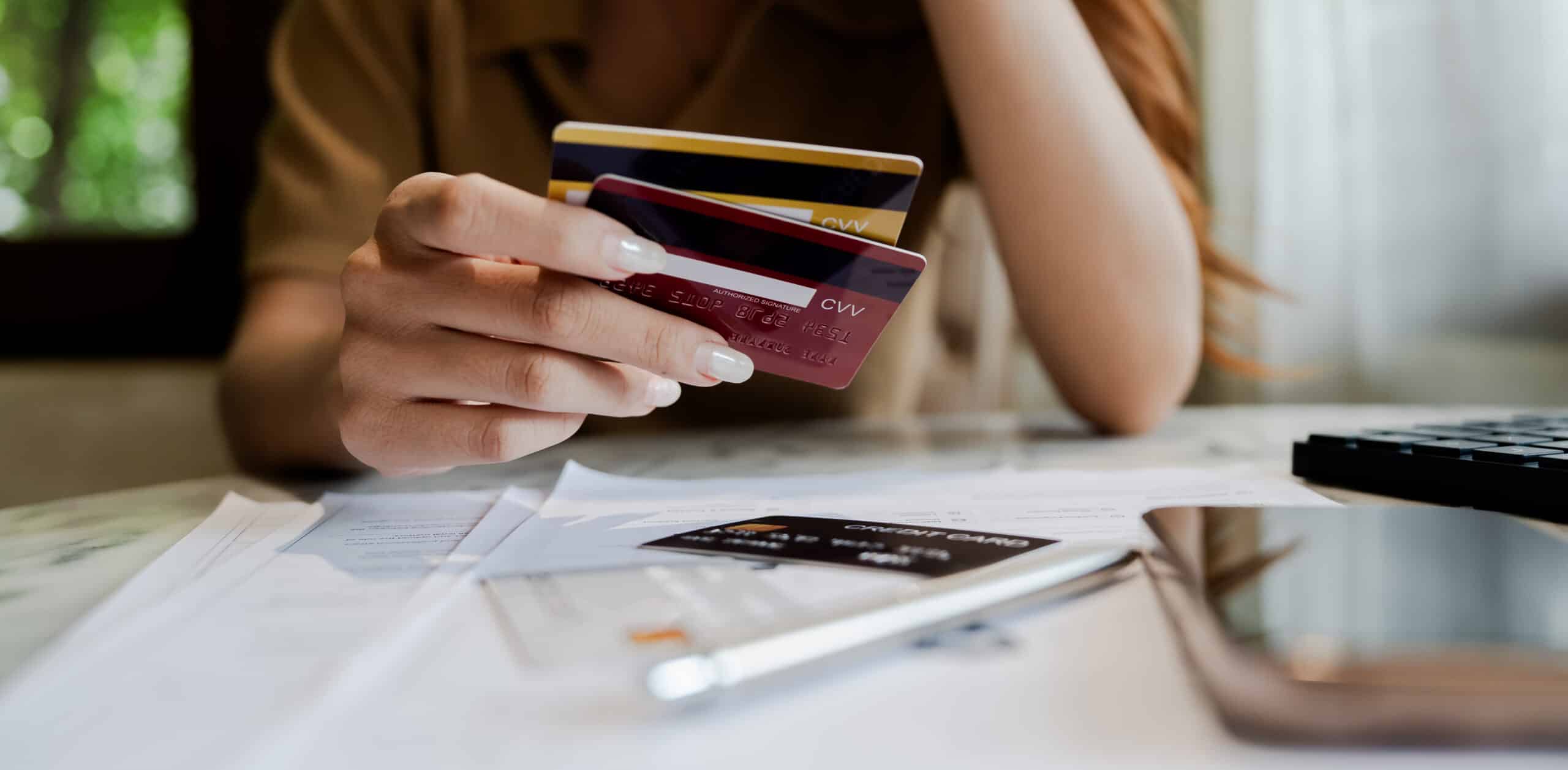 Kreditlinien und Karten: Kosten und Rückzahlung im Blick Person hält zwei Kreditkarten in der Hand, auf dem Tisch liegen Rechnungen und ein Taschenrechner