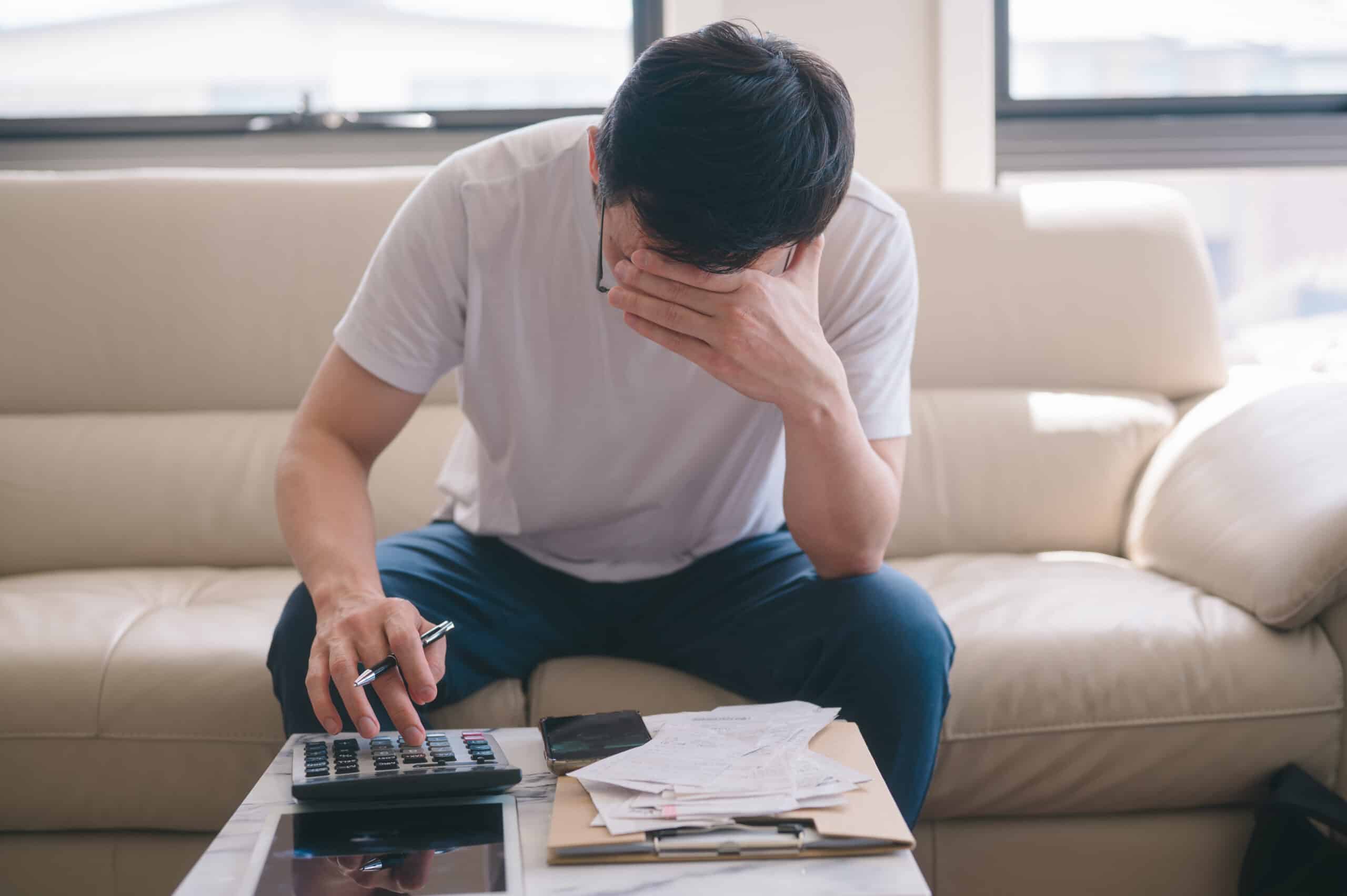 Überschuldung: Wenn die Rechnungen nicht mehr aufgehen Mann sitzt mit Taschenrechner und einem Stapel Rechnungen und stützt sorgenvoll den Kopf