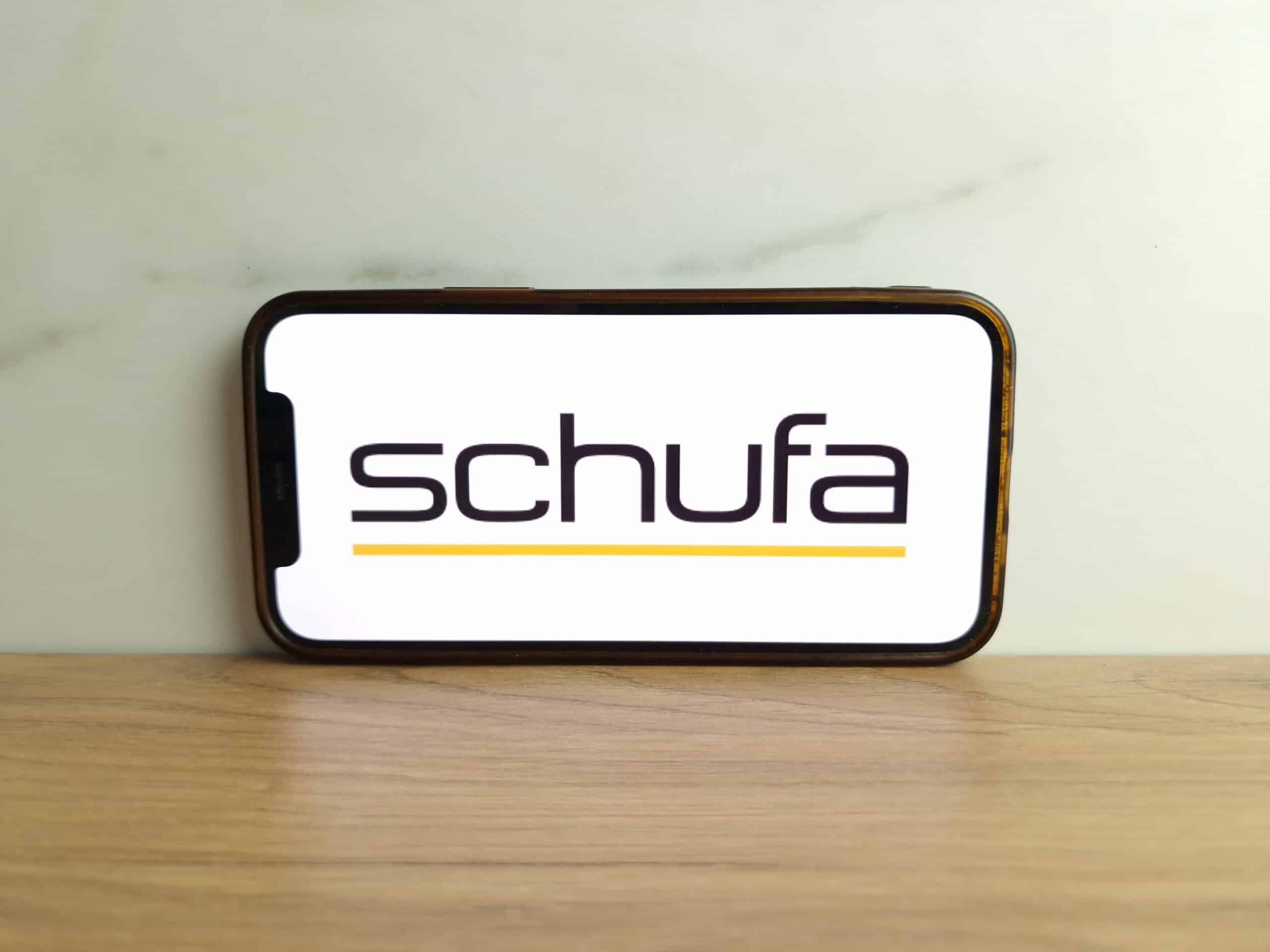 Wie funktioniert die SCHUFA? SCHUFA-Logo auf dem Smartphone Smartphone mit SCHUFA-Logo auf dem Display, aufgestellt vor heller Wand