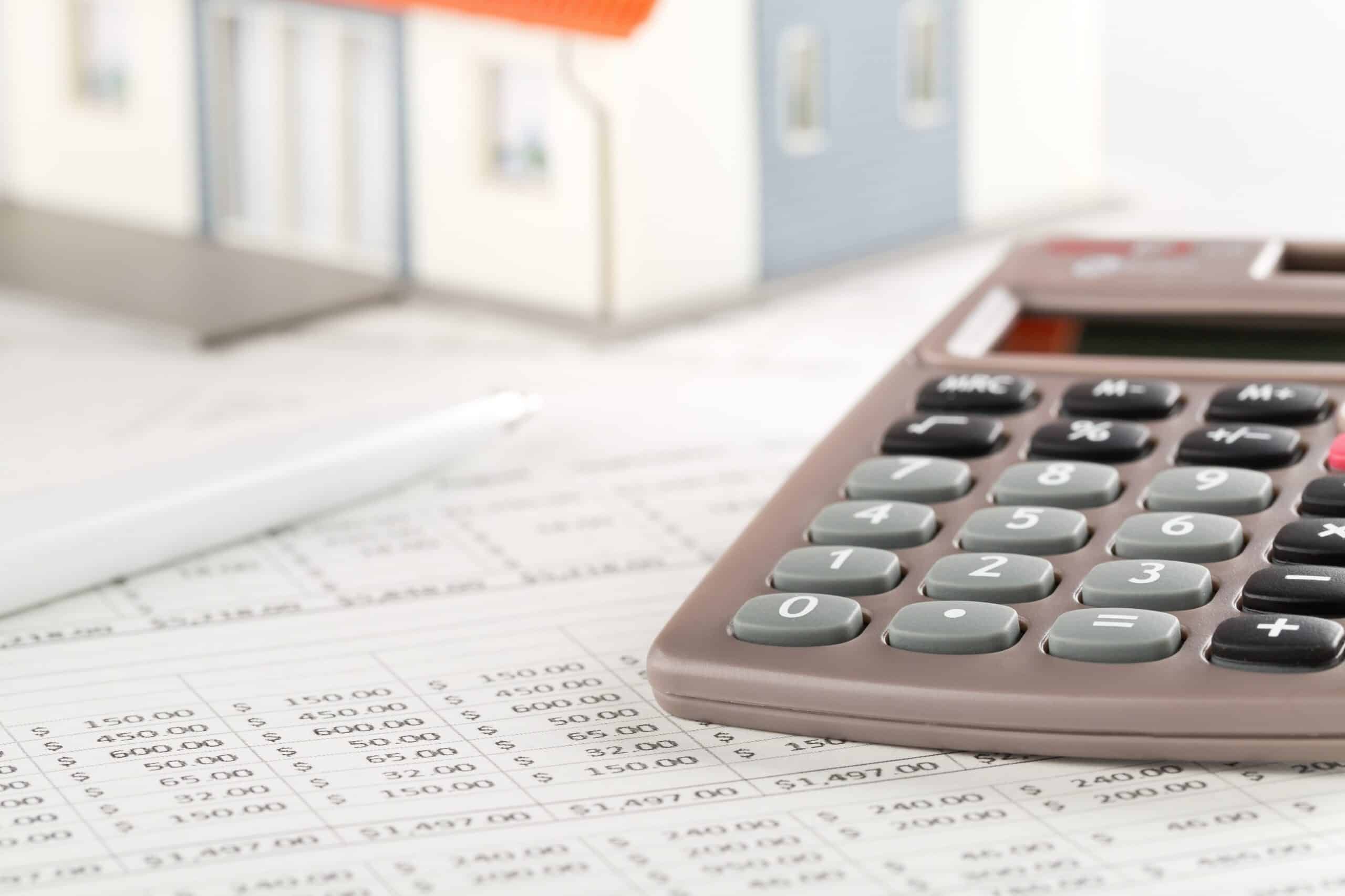 Tilgungsplan prüfen: Grundlage der Vorfälligkeitsentschädigung Taschenrechner und Stift auf einer Tilgungs- und Zinstabelle, im Hintergrund ein Hausmodell