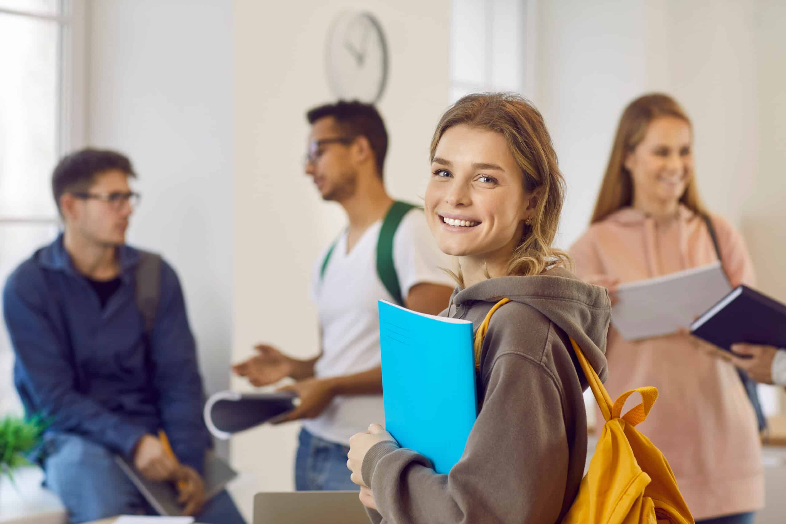 Studienfinanzierung Studierende Hochschule Alltag Lächelnde Studentin mit Heft und Rucksack in einer Gruppe Studierender
