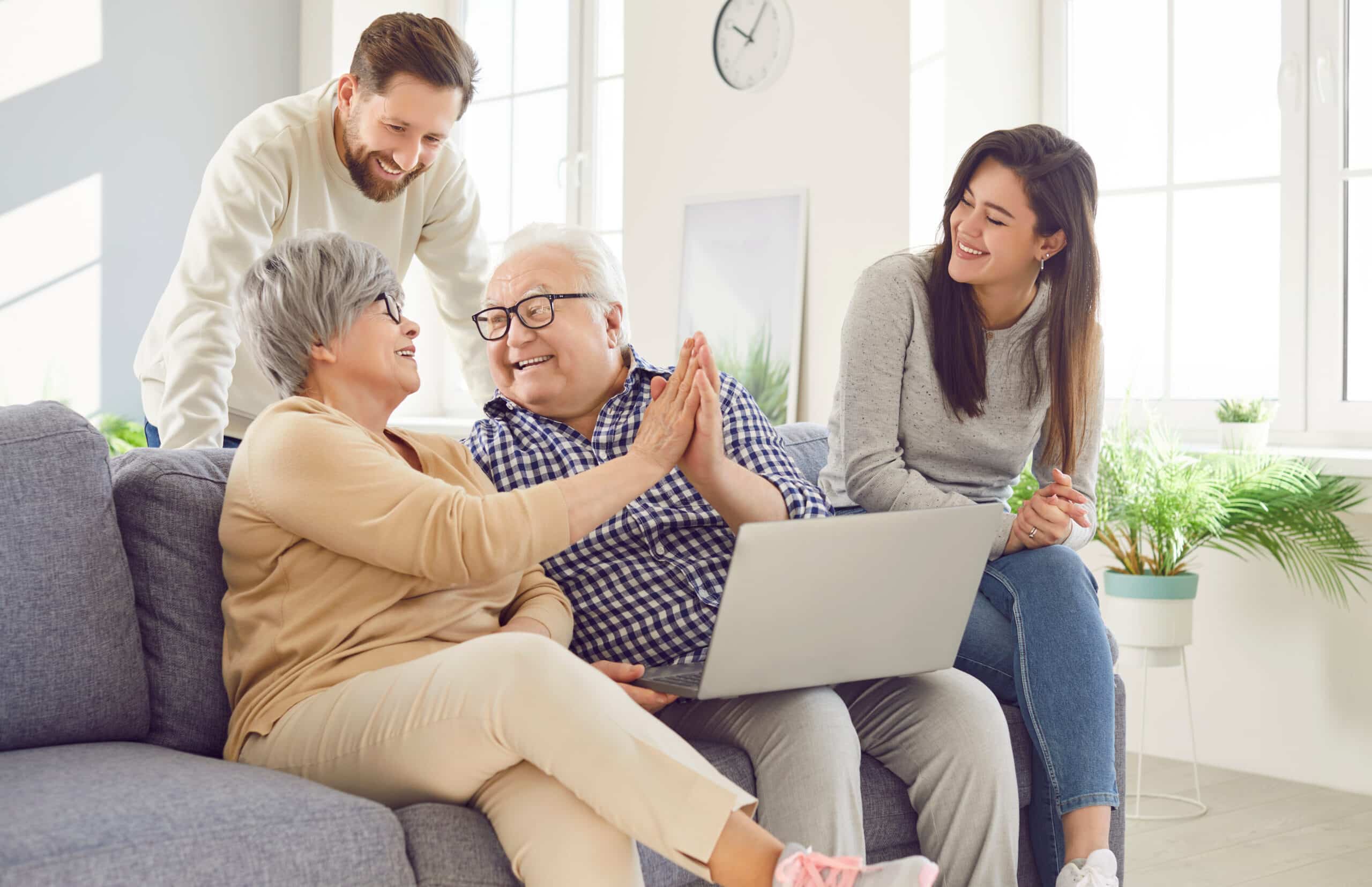 Vermögensnachfolge in der Familie: Immobilie übertragen Fröhliche Familie aus zwei Generationen sitzt mit Laptop auf dem Sofa und bespricht Unterlagen