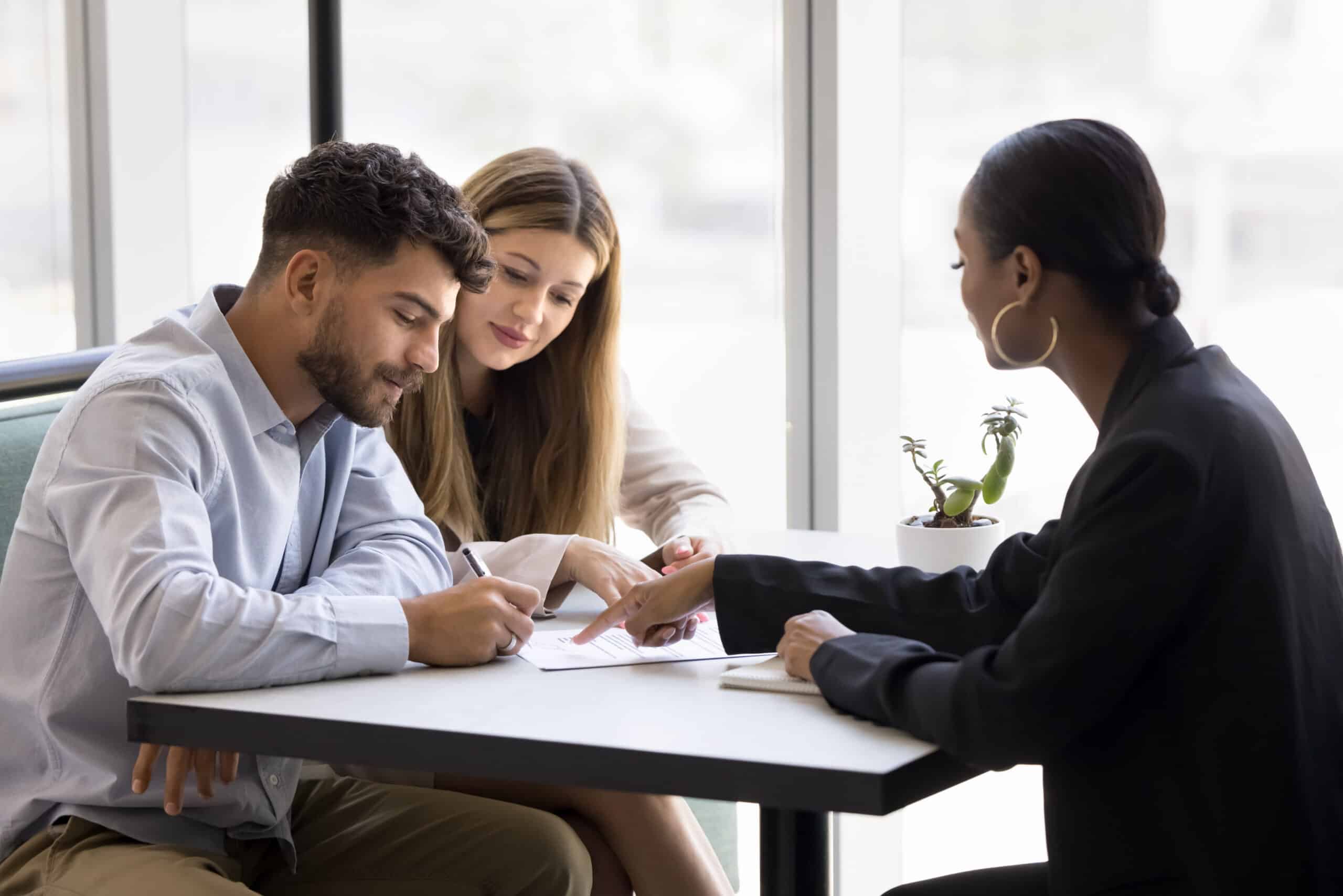 Grundschuldbestellung unterschreiben: Konditionen klären Junges Paar unterschreibt im Beratungsgespräch einen Vertrag, die Beraterin zeigt auf die Unterlagen